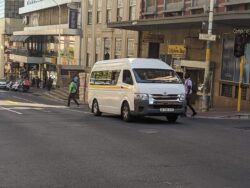 A van operating as a jitney waits on a city street in a commercial area.