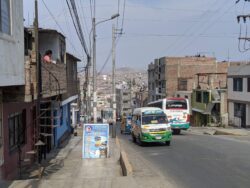 Minibuses wait along a street with informal, hastily built homes where businesses also exist.