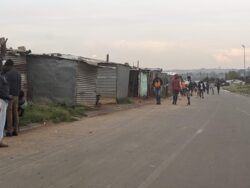 On a street in Johannesburg, people reside in densely-spaced shacks.