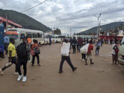 Riders wait near a minbus terminal in Kigali, with multiple buses stationed.