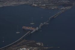 Aerial view of the collapsed Francis Scott Key Bridge in Baltimore, with the cargo ship still in position, obstructing access.
