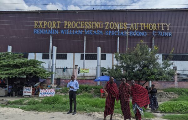 Men in tribal gear stand outside an export processing facility.