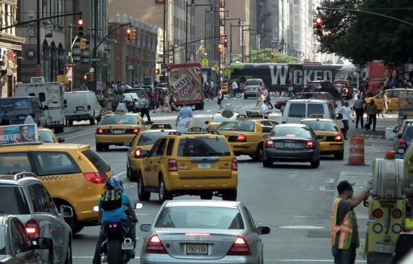 A congested street in New York City, with taxicabs merging into the street and pedestrians looking on.